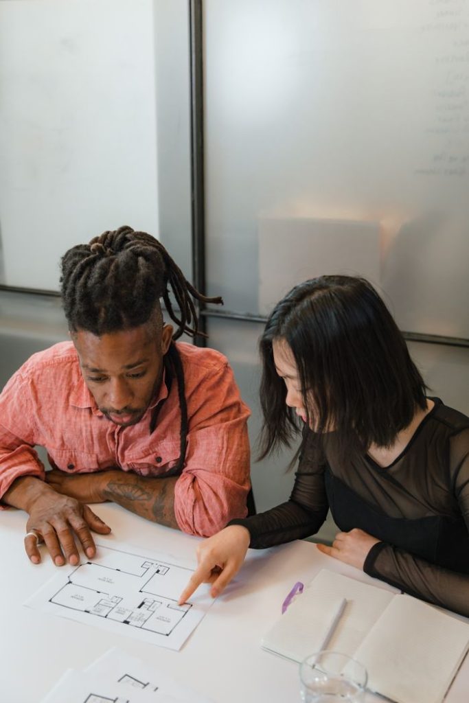 Two colleagues discussing floor plans during a business meeting in a modern office setting.