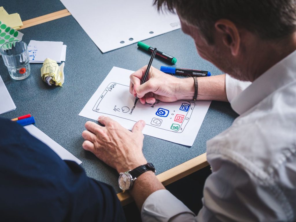Crafting Captivating Headlines: Your awesome post title goes here A designer sketches a mobile app prototype on paper at an office desk, focusing on creativity and design.